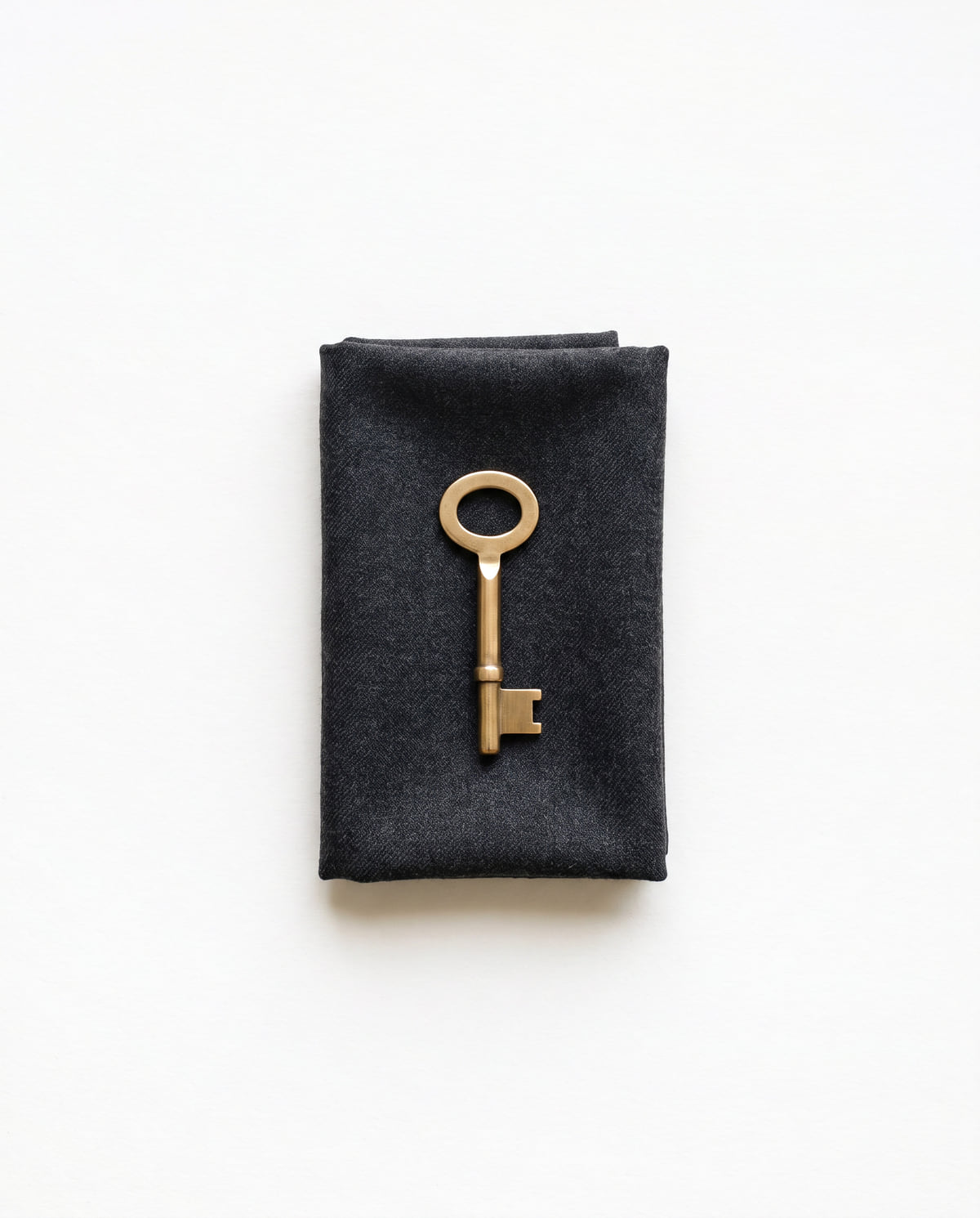 A single brass key resting on folded charcoal wool.