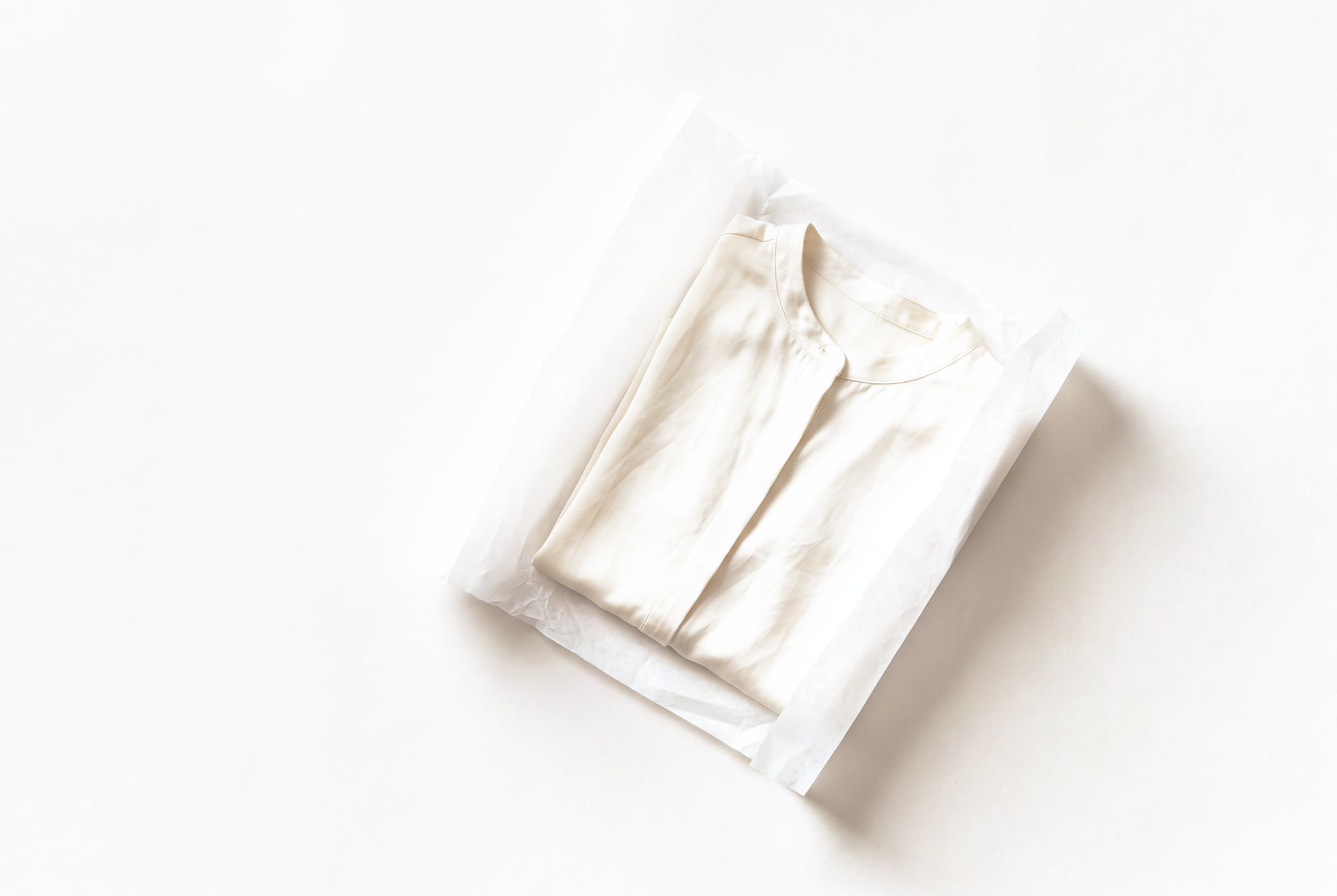 An ivory silk blouse half-wrapped in white tissue paper, the tissue folded back and left open.